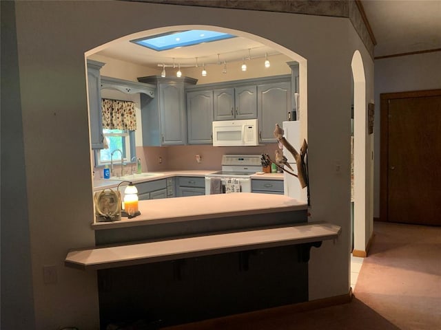 kitchen featuring sink, white appliances, gray cabinets, and a skylight