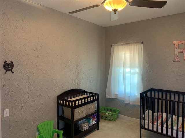 bedroom with ceiling fan, a nursery area, and carpet flooring