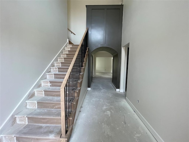 stairway with baseboards, arched walkways, and concrete flooring