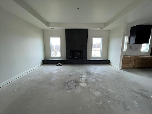 unfurnished living room with a tray ceiling, a large fireplace, baseboards, and unfinished concrete flooring