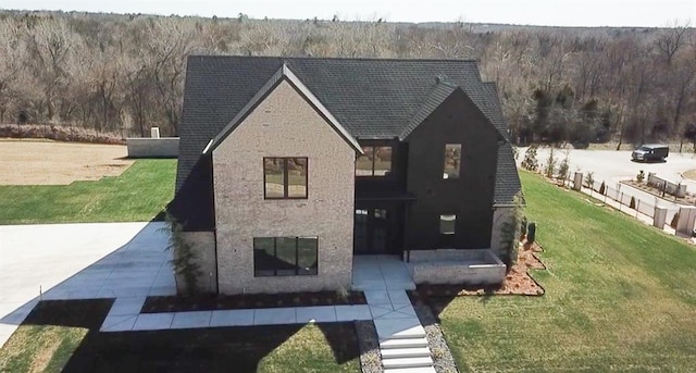 view of front of house featuring brick siding, a wooded view, and a front yard