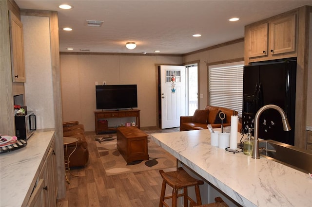 kitchen featuring black fridge with ice dispenser, a sink, open floor plan, light wood-type flooring, and visible vents