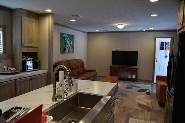 kitchen featuring open floor plan, stainless steel microwave, a sink, freestanding refrigerator, and wood finished floors
