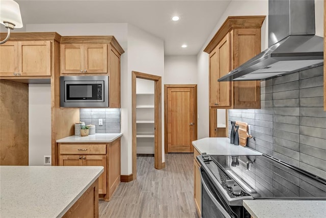 kitchen featuring tasteful backsplash, light stone counters, wall chimney exhaust hood, stainless steel appliances, and light hardwood / wood-style floors