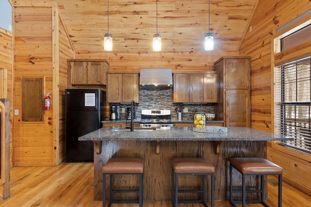 kitchen featuring lofted ceiling, wall chimney exhaust hood, black refrigerator, dark stone countertops, and light wood-type flooring