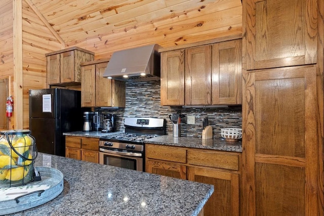 kitchen with tasteful backsplash, dark stone countertops, black fridge, wall chimney exhaust hood, and gas range