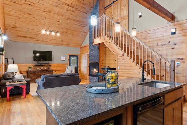 kitchen with dark stone countertops, wood walls, sink, black dishwasher, and high vaulted ceiling