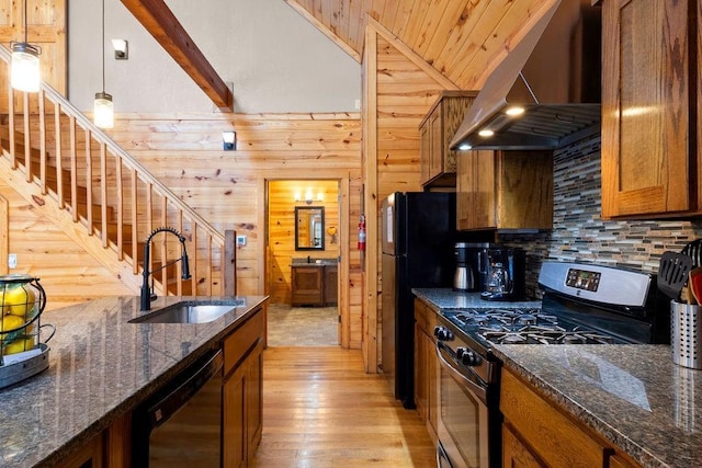 kitchen with decorative light fixtures, wall chimney range hood, black dishwasher, wooden walls, and stainless steel gas stove