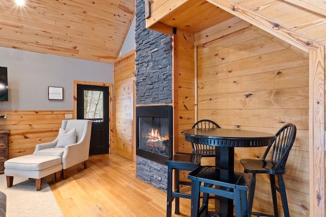 sitting room featuring wood ceiling, wood walls, a stone fireplace, high vaulted ceiling, and light hardwood / wood-style flooring