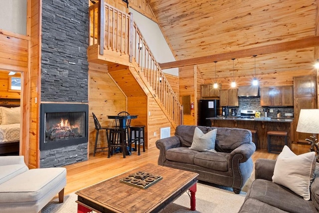 living room with wood walls, light hardwood / wood-style flooring, a stone fireplace, high vaulted ceiling, and wooden ceiling