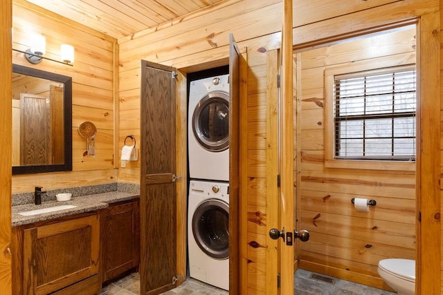 laundry room with sink, stacked washer / dryer, and wooden walls