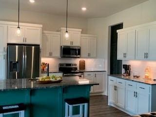 kitchen with a breakfast bar area, white cabinets, pendant lighting, and appliances with stainless steel finishes