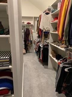 walk in closet with light colored carpet and lofted ceiling