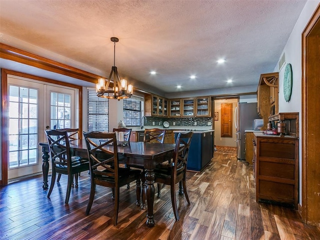 dining area with a textured ceiling, an inviting chandelier, dark hardwood / wood-style floors, and french doors