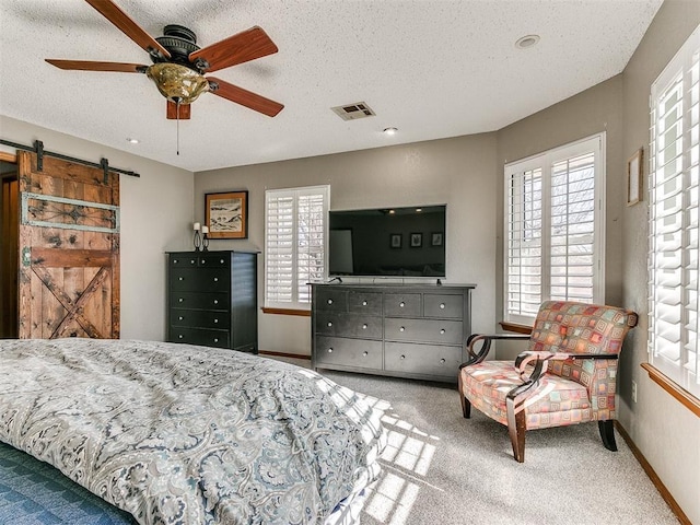 bedroom featuring ceiling fan, a barn door, carpet floors, and a textured ceiling