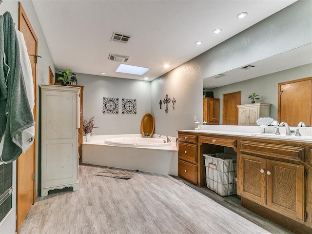 bathroom featuring a bathtub, vanity, a skylight, and hardwood / wood-style flooring