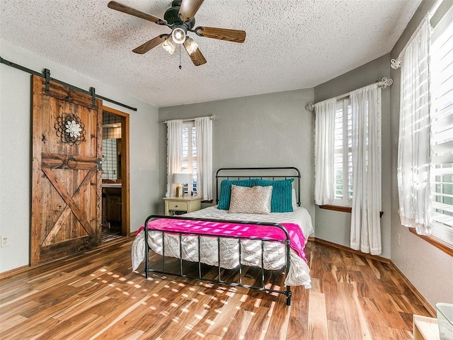 bedroom with a textured ceiling, ceiling fan, a barn door, and wood-type flooring