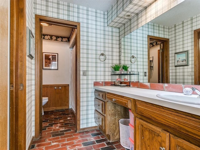 bathroom featuring a textured ceiling, toilet, vanity, and wooden walls