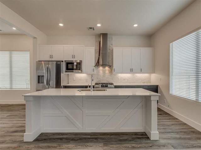 kitchen with wall chimney range hood, stainless steel fridge, a kitchen island with sink, and built in microwave