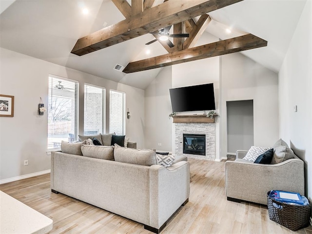 living room featuring light wood-type flooring, ceiling fan, beam ceiling, and a stone fireplace