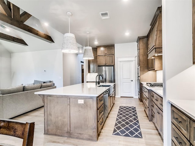 kitchen with a large island with sink, appliances with stainless steel finishes, decorative light fixtures, backsplash, and lofted ceiling with beams