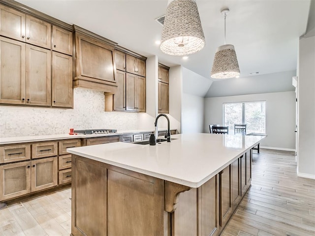 kitchen featuring a kitchen bar, an island with sink, lofted ceiling, hanging light fixtures, and sink