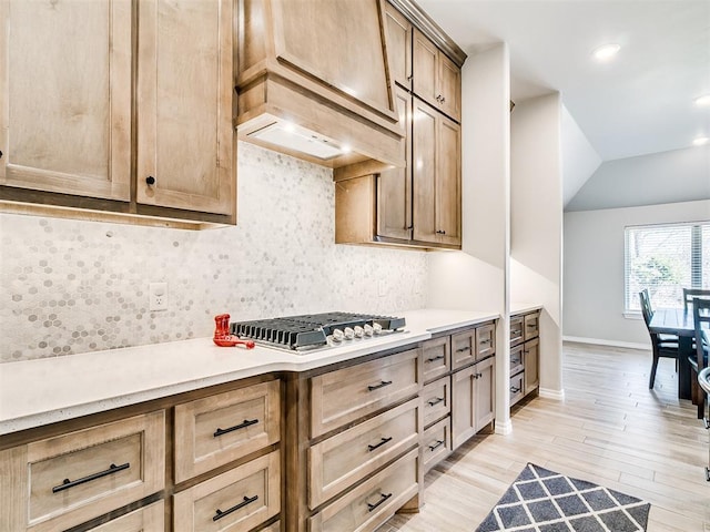 kitchen featuring lofted ceiling, premium range hood, backsplash, stainless steel gas cooktop, and light wood-type flooring