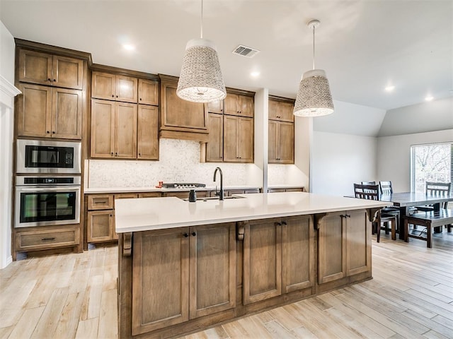 kitchen featuring hanging light fixtures, vaulted ceiling, stainless steel appliances, and a center island with sink