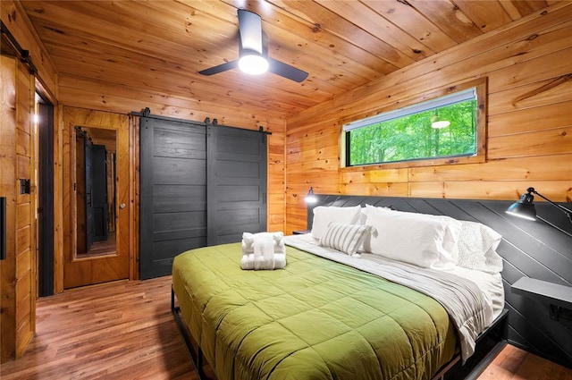 bedroom featuring hardwood / wood-style flooring, wooden walls, a barn door, ceiling fan, and wooden ceiling