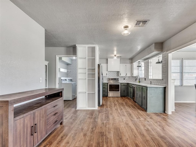 kitchen with light hardwood / wood-style floors, white cabinetry, washer / clothes dryer, appliances with stainless steel finishes, and sink