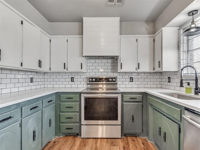 kitchen with appliances with stainless steel finishes, light wood-type flooring, decorative backsplash, sink, and white cabinetry