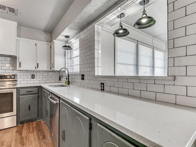 kitchen featuring appliances with stainless steel finishes, pendant lighting, decorative backsplash, sink, and white cabinetry