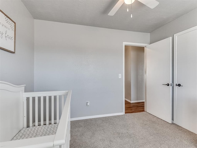 unfurnished bedroom featuring a crib, ceiling fan, and carpet