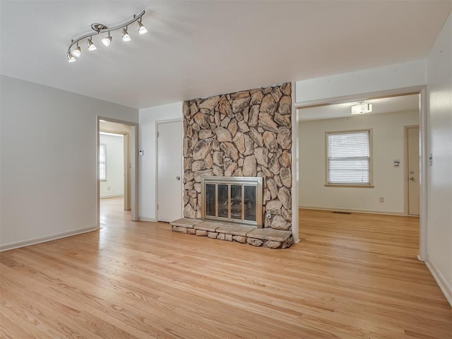 unfurnished living room with light hardwood / wood-style flooring, a stone fireplace, and a wealth of natural light