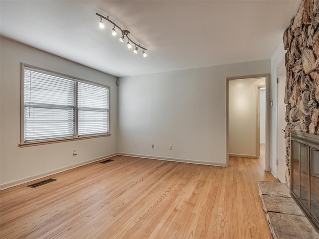 spare room with rail lighting, light hardwood / wood-style floors, and a fireplace