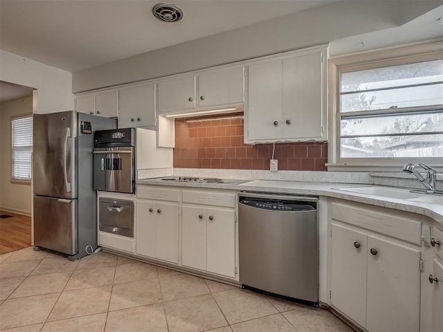 kitchen with sink, decorative backsplash, light tile patterned floors, appliances with stainless steel finishes, and white cabinetry