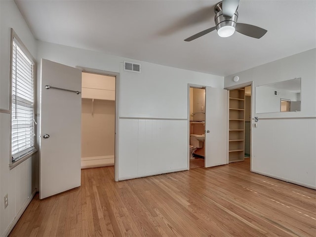 unfurnished bedroom with ensuite bathroom, a walk in closet, ceiling fan, light wood-type flooring, and a closet