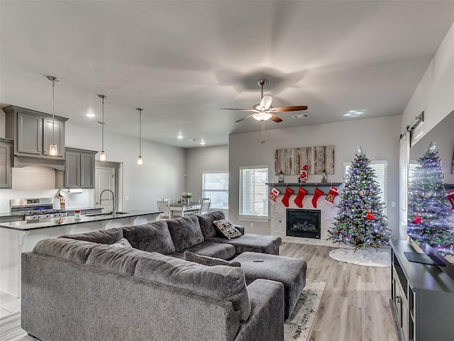 living room featuring ceiling fan, a barn door, light hardwood / wood-style floors, and sink