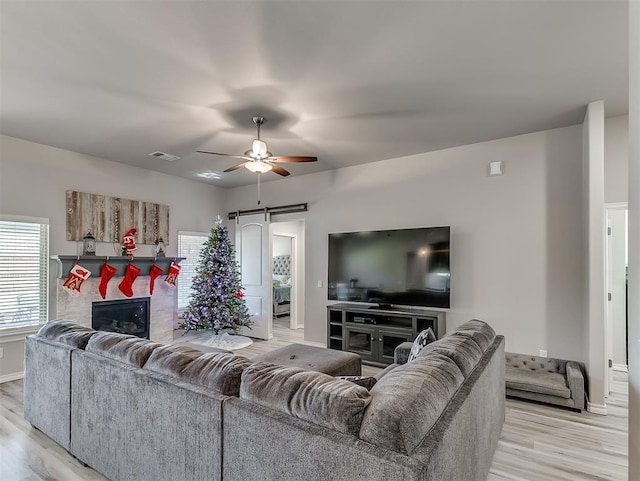 living room featuring ceiling fan, a barn door, and light hardwood / wood-style flooring