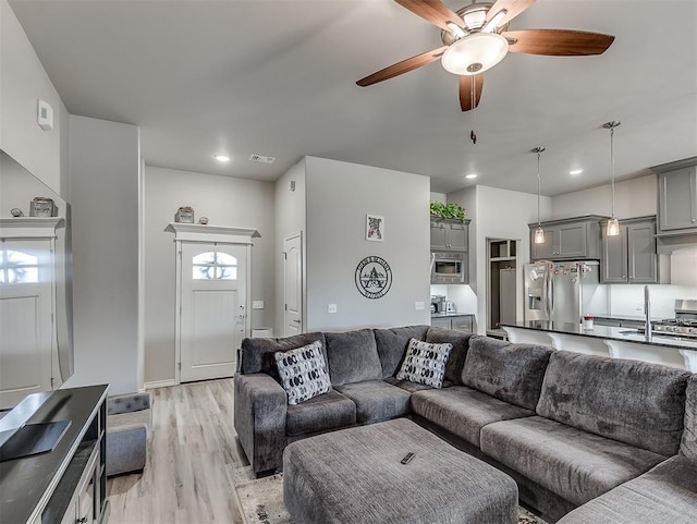 living room featuring sink, ceiling fan, light wood-type flooring, and a healthy amount of sunlight