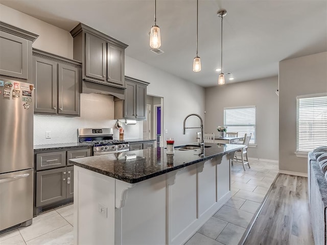 kitchen with decorative light fixtures, a kitchen island with sink, appliances with stainless steel finishes, dark stone countertops, and sink