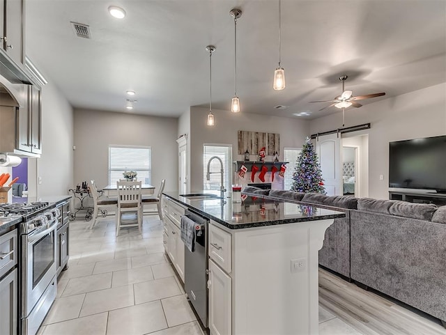 kitchen featuring a kitchen island with sink, a barn door, stainless steel appliances, sink, and white cabinetry