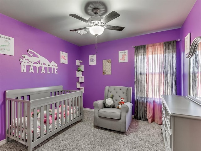 carpeted bedroom with a crib and ceiling fan