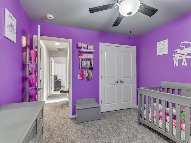 bedroom featuring a closet, ceiling fan, a crib, and light carpet