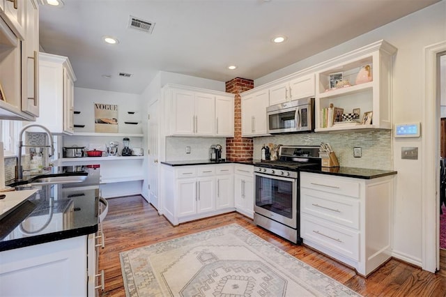 kitchen with appliances with stainless steel finishes, light hardwood / wood-style floors, decorative backsplash, sink, and white cabinetry