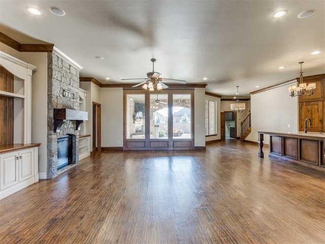 unfurnished living room featuring sink, hardwood / wood-style flooring, a fireplace, and ceiling fan with notable chandelier