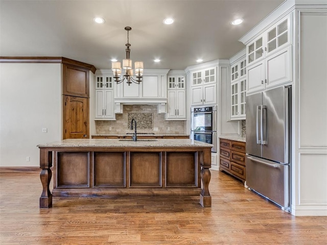 kitchen featuring stainless steel appliances, light stone counters, white cabinets, a center island with sink, and decorative light fixtures