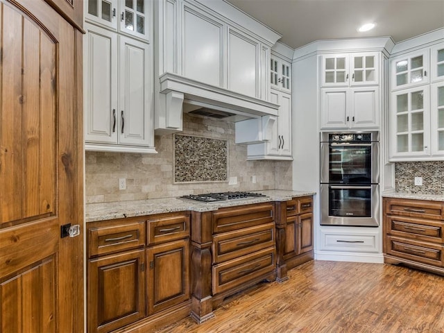 kitchen with light stone counters, appliances with stainless steel finishes, light hardwood / wood-style floors, and white cabinets