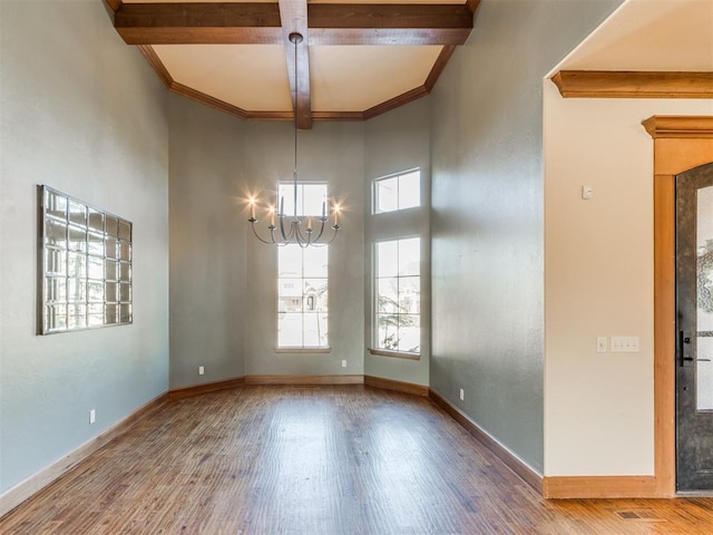 empty room with hardwood / wood-style flooring, an inviting chandelier, beam ceiling, a towering ceiling, and coffered ceiling