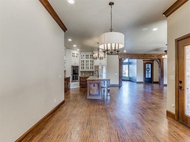 kitchen featuring crown molding, a breakfast bar, a kitchen island with sink, hanging light fixtures, and dark hardwood / wood-style flooring